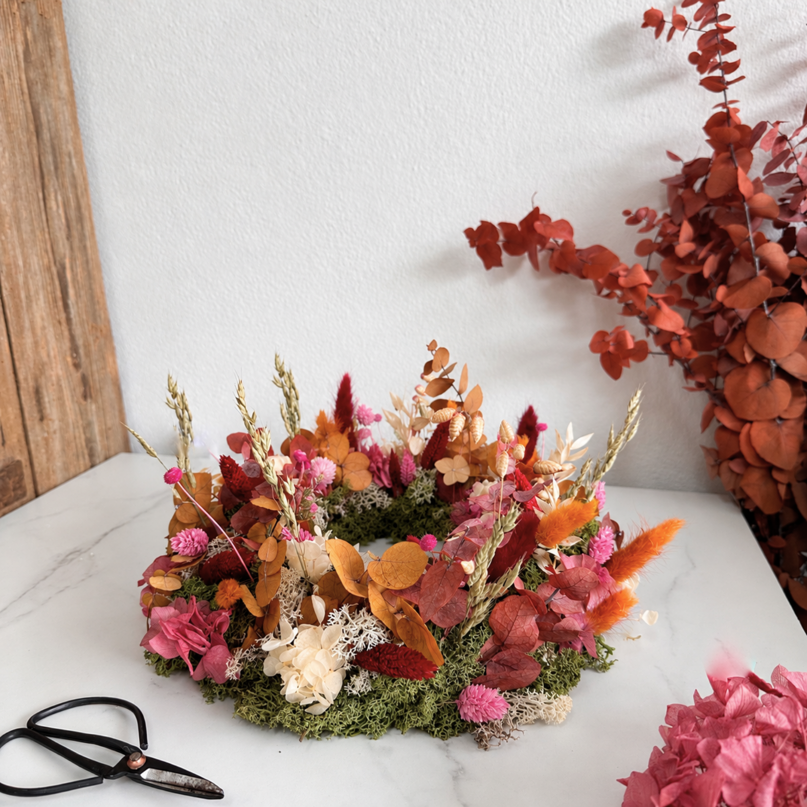 Tischkranz Nele seitlich: Herbstkranz aus Trockenblumen mit Gräsern und Eukalyptus auf Marmor